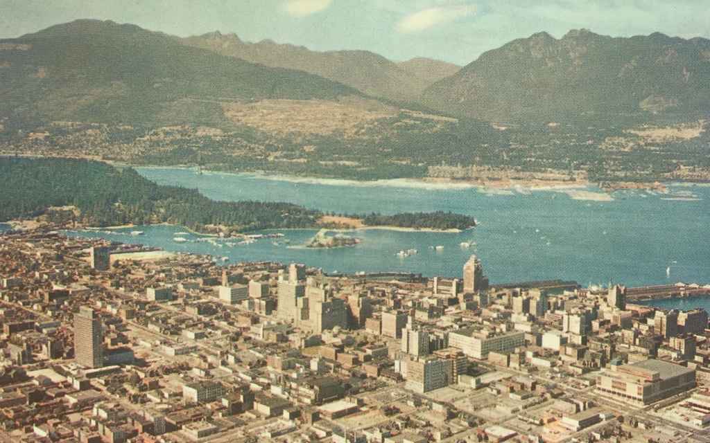 Mid 1950s aerial view of Vancouver BC and Harbour, showing the busy West Georgia Street running east to west with the then new Post Office building in the lower right corner. (Postcard published by Natural Color Productions Ltd., Vancouver, B.C.)